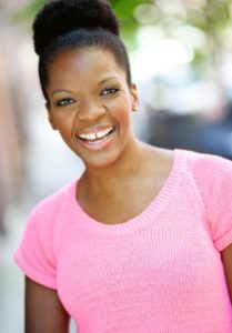 A woman in a pink sweater-shirt smiles for the camera